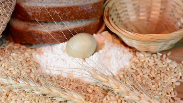 Wheat grains, wheat ears, flour, eggs and bread slices on wooden table