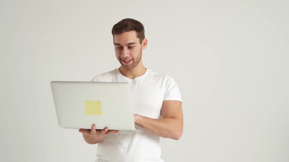 Studio Portrait of Happy Smiling Young Man Using Laptop Computer to Browse Internet Advertising