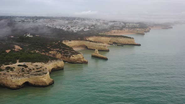 Fontainhas Galé Beach in the south of Portugal on a foggy morning showing eroded cliffs, Aerial pan