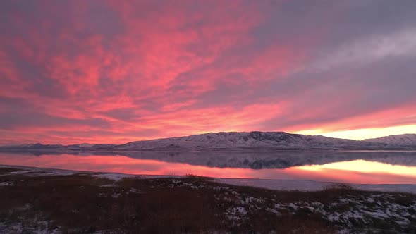 Aerial view flying past trees and over Utah Lake with colorful sunset