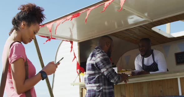 Smiling mixed race woman using smartphone waiting in queue to be served at food truck