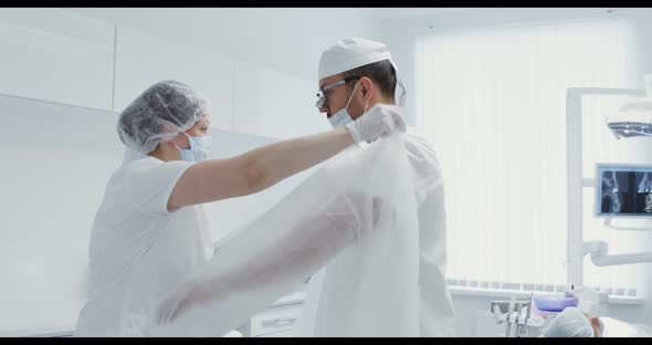 A Nurse Helps a Dentist Put on a White Sterile Suit Tying the Ties of His Back