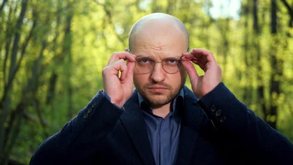 A Bald Elegant Male Scientist Puts on Glasses and Looks at the Camera