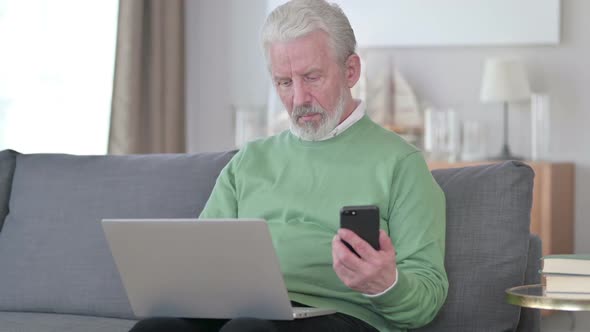 Attractive Old Man Working on Smartphone and Laptop