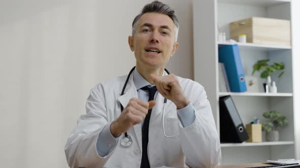 Confident caucasian male MD wearing medical gown giving online consultation, holding video call