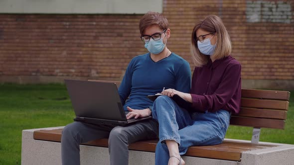 Two professional coworkers in protective mask discuss concentrating typing on laptop