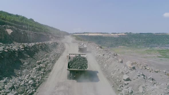 Mining Dump Trucks in Large Granite Open Pit Mine. Loaded Trucks Rides on Road Quarry Ledge Drone