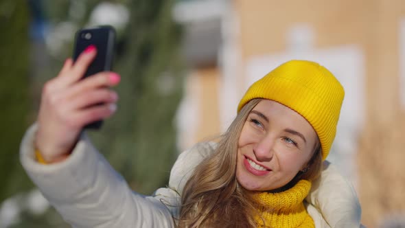 Charming Young Millennial Woman Taking Selfie on Smartphone Standing on Sunny Winter Resort Outdoors