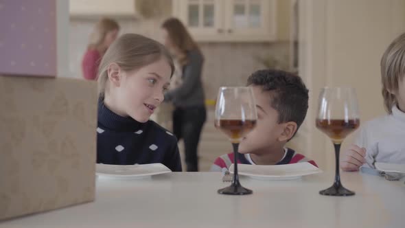 Portrait Three Funny Kids Sitting at the Table with Small Cake and Wine Glasses with Juice