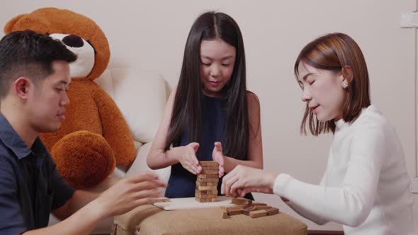 Asian mother, father, and pretty daughter playing wooden block tower together