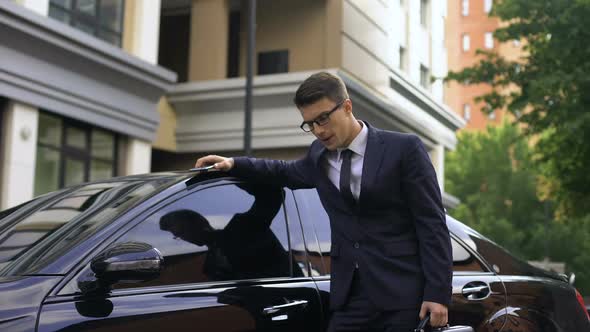 Upset Young Businessman Standing Near Luxurious Car, Talking on Phone, Bad News