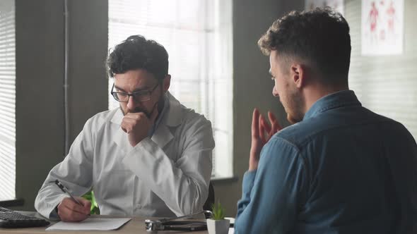 Young Male Patient at the Reception of a Young Doctor in the Office at the Table