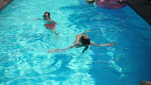 Wide Shot of Happy Caucasian Kids Lying on Back in Azure Blue Water in Swimming Pool Talking and