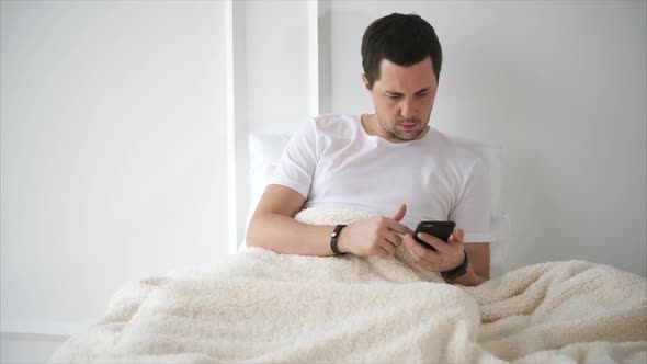 Handsome Man Is Lying in Bed with Smartphone