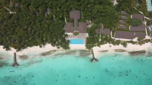 Top view of a hotel with a jetty in the Maldives island with many green plants and breakwaters.