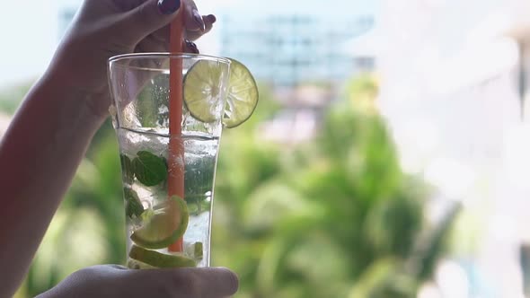 Woman Stirs Cold Mojito Cocktail with Orange Straw