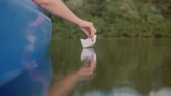 Handsome Girl Launching Origami Ship In Water On Sunset. Relaxing And Enjoying Time. Paper Boat.