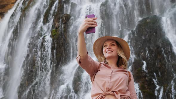 Woman Taking a Selfie on the Background of a Waterfall