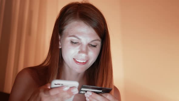 Smiling Woman Sitting on Bed with Wireless Laptop and Using Mobile with Credit