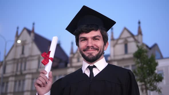 Caucasian Happy Young Graduated Man Posing To the Camera and Showing His Diploma in Front of the