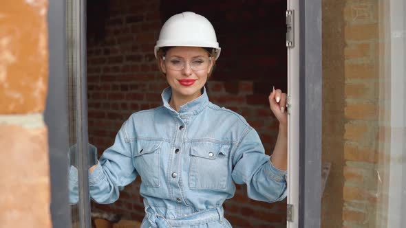 A Female Architect or Bricklayer Stands in an Open Window at a Construction Site