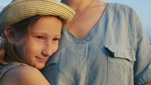 A Beautiful Blonde Girl in a Hat Clung to Her Mother's Chest