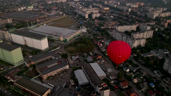 Red Hot Air Balloon Flying Over Buildings in Industrial Zone in Small European City at Summer Sunset