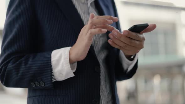 Close up Asian businesswoman in a black suit is using a smartphone texting.