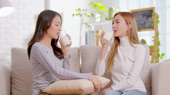 Smiling Asian women are drinking glasses of milk and looking at each other