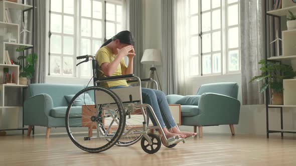 Disappointed Asian Kid Girl Sitting In A Wheelchair In Living Room At The House