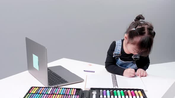 Girl drawing with wax gis in notebook with blank leaves. Showing your camera drawing.