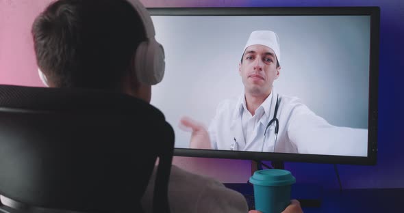 Rear View of Young Man Watching Video Online Conference with Doctor