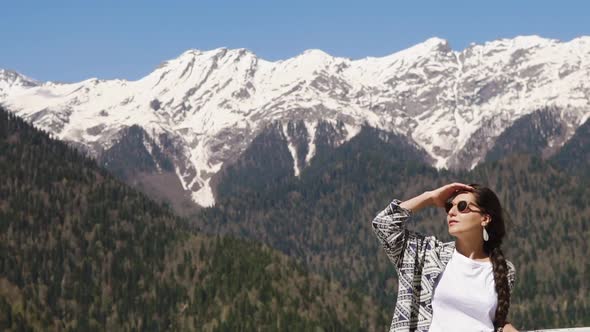 Relaxed Traveler Woman Is Standing in Background of Mountains in Sunny Day