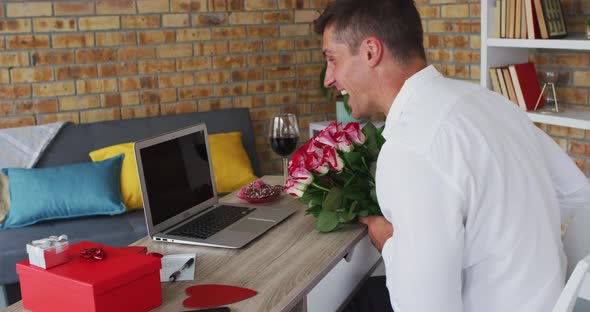 Caucasian man making video call using laptop holding bunch of flowers and blowing kiss