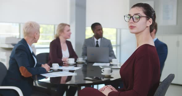 Portrait of Attractive Businesswoman Looking at Camera Sitting at Conference Room with Colleagues