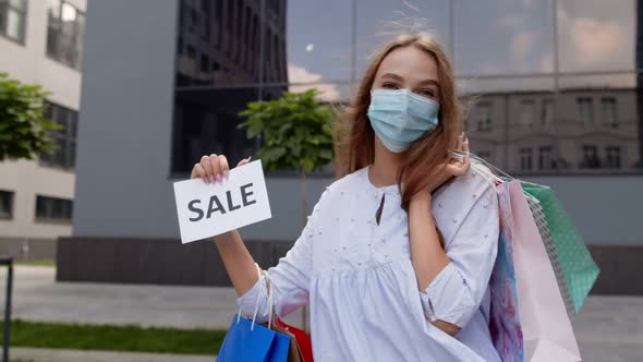 Girl in Protective Mask with Shopping Bags Showing Sale Word Inscription During Covid-19 Pandemic