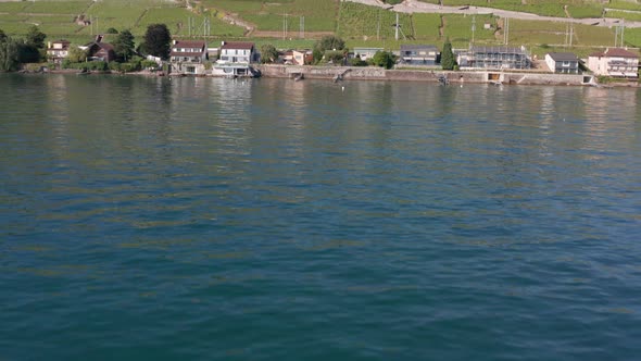 Drone flying over Geneva lake, tilting up and flying over beautiful lakeside houses