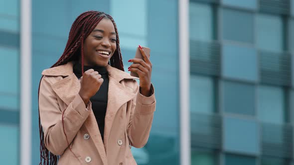 Happy Millennial African American Woman Standing Outdoor on Modern Building Background Holding