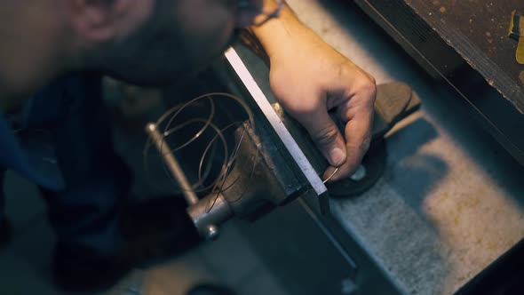 Jeweler Pulls Gold Wire Through Tool in Bench Clamp Closeup