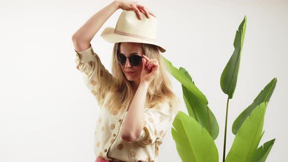 Lovely Caucasian Blonde Girl with Black Sunglasses and Hat Looking Into the Camera White Background