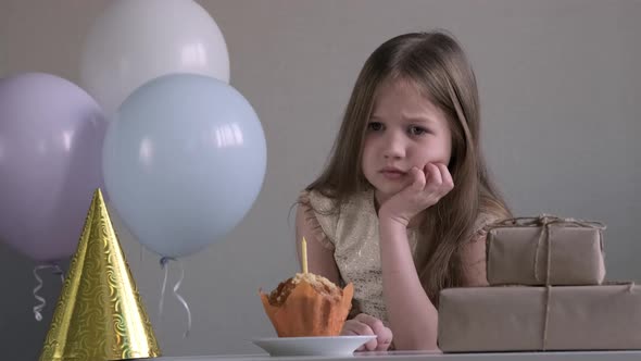 Sad Little Girl Celebrating Birthday Alone Over Background of Gifts and Balloons