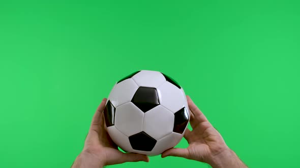 Male Hands Holding a Classic Black and White Soccer Ball Isolated on Studio Green Screen of Key