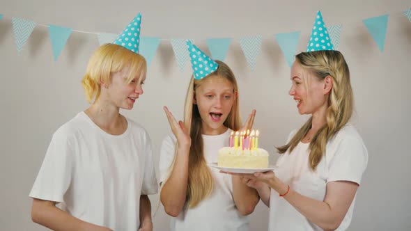 Happy Girl with Sister and Mom Celebrate Birthday By Blowing Out Candles on Cake and Clapping Hands