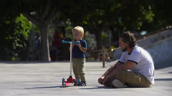 Father with His Little Son in the Skatepark About to Traing Skating on the Scooter