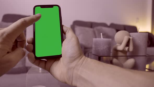 Pov close up male person touching and swiping mobile phone with green screen indoors