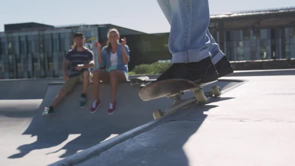 Caucasian woman and man cheering their skateboarding friend on sunny day