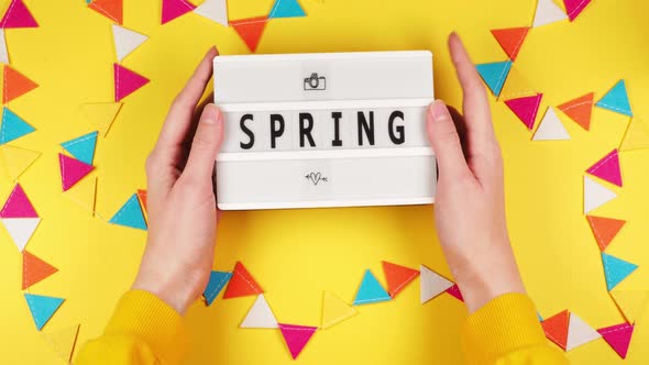 Hands of a young girl in a sweater hold a white board with the inscription Spring