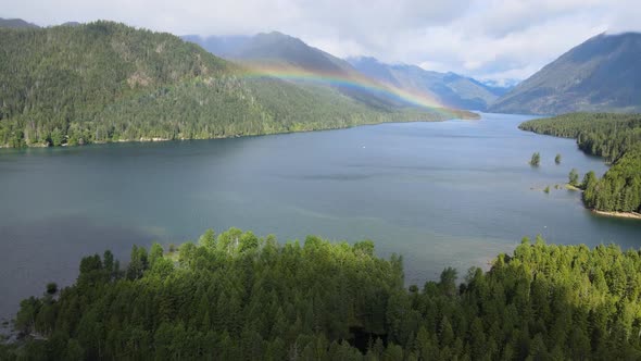 Natural rainbow in valley, lush rainforest, green trees, mountain hills, sunny day with clouds