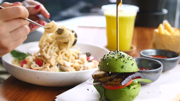 Closeup Female Hands Eating Pasta And Avocado Burger In Vegan Cafe