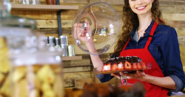 Portrait of smiling waitress holding cake at counter